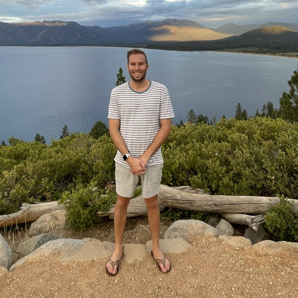 Sam Mesquita standing in front of lake with mountains in background