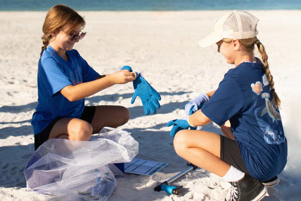 Two young girls putting on gloves for beach cleanup