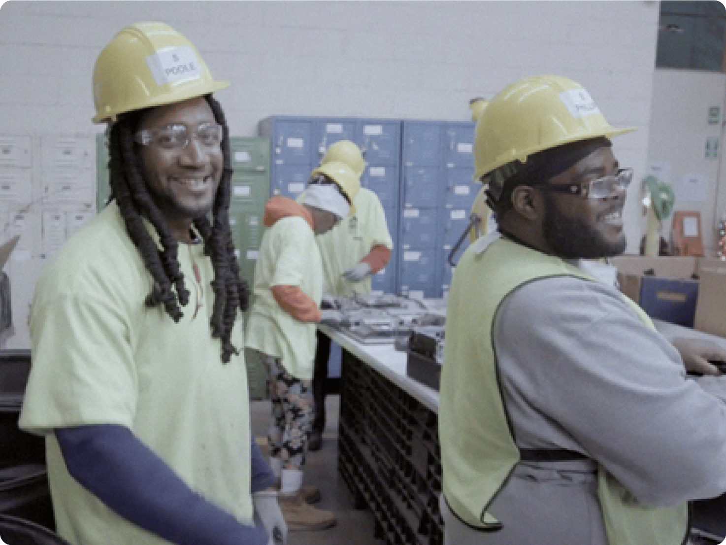Two men wearing hard hats and safety vests inside a recycling facility.