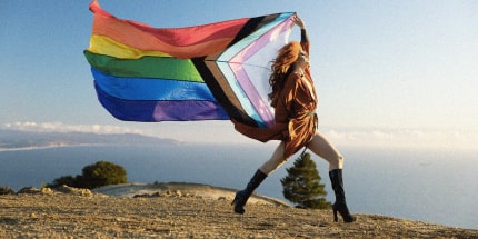 Drag queen holding a Pride flag in the mountains