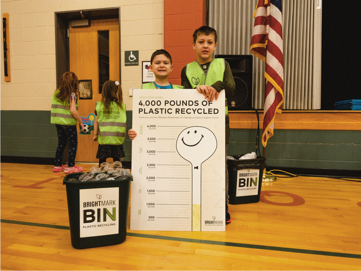 Two kids holding up a graph that tracks how much plastic waste their school has recycled.